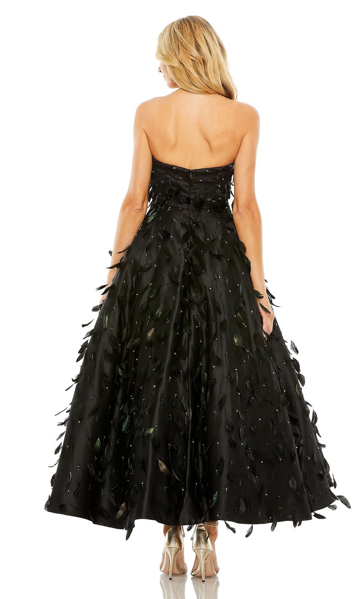 A woman models the Strapless Midi Formal Dress: Mac Duggal 11634, an ankle-length black gown with leaf-inspired details, standing with her back to highlight its elegant design.